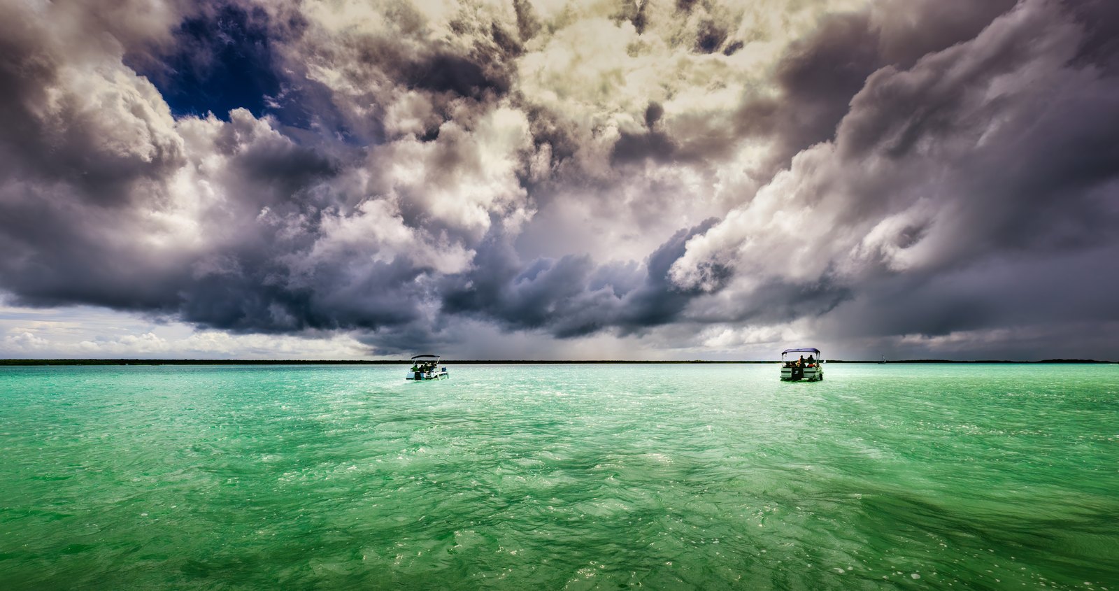 Türkisfarbenes Wasser trifft am niedrigen Horizont auf eine mächtige, dunkel aufgetürmte Wolkenfront.