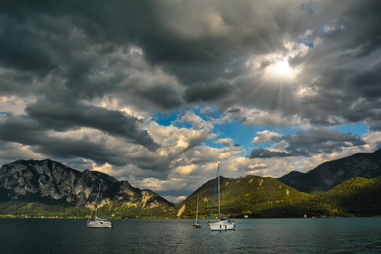 Lichtstrahlen fallen durch schwere Wolken auf einen Bergsee mit kleinen Segelbooten.
