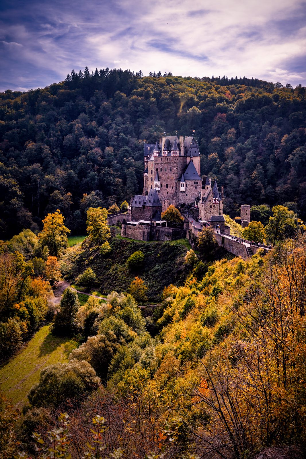 Burg Eltz liegt von herbstlichem Wald umgeben in einer bewaldeten Hügellandschaft.